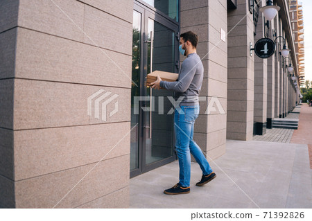 Delivery man wearing medical mask ringing door for delivery carton boxes with hot pizza. 71392826