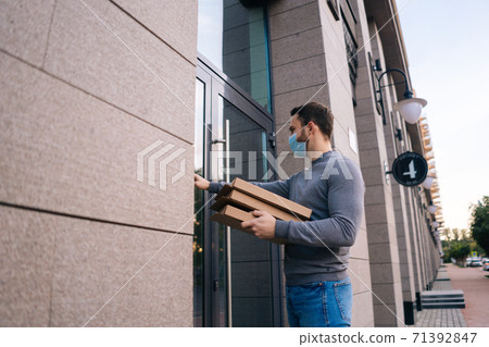 Delivery man wearing medical mask ringing door for delivery carton boxes with hot pizza. 71392847