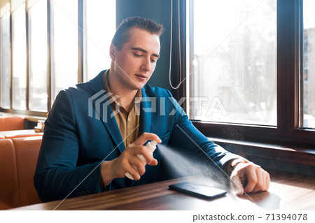 Young caucasian guy businessman in a blue suit sprays an antiseptic on a mobile phone 71394078
