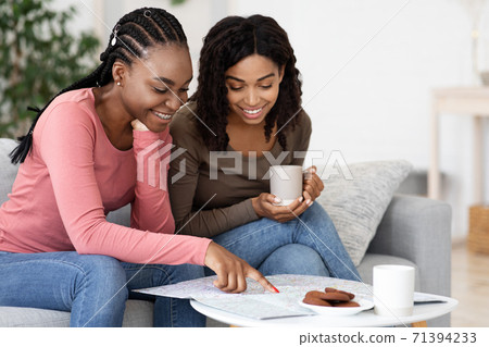 Joyful african american girlfriends looking at map while drinking coffee 71394233