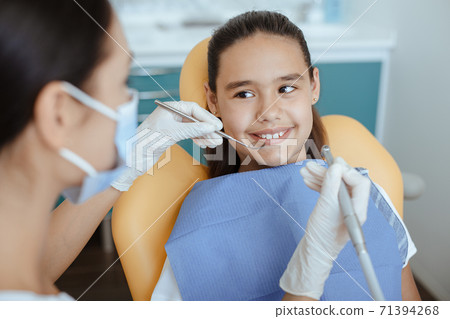 Millennial female doctor in protective mask and glove holds medical instrument and checks oral cavity 71394268