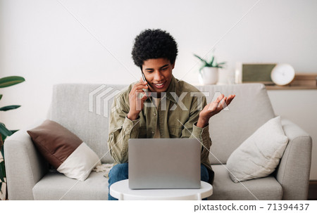 Distance learning concept. Happy black teenager talking on mobile phone in front of laptop at home Distance learning concept. Happy black teenager talking on mobile phone in front of laptop at home 71394437
