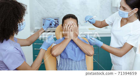 Little cute girl closing her face with hands, preventing examination of teeth, of fear of doctor Little cute girl closing her face with hands, preventing examination of teeth, of fear of doctor 71394659