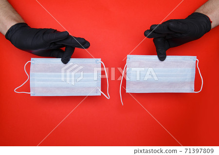 hands in black latex gloves hold two medical masks, one with torn elastic band hands in black latex gloves hold two medical masks, one with torn elastic band 71397809