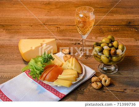 Cheese, salad, olives, onions and gherkins in a vase, a glass of wine and a white napkin 71399736