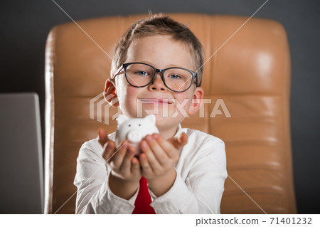 Child calculates savings with pig bank in his hands. Child businessman with earned money in big bag. Ideas how to earn money. Funny little kid boss sitting in leather armchair with laptop Child calculates savings with pig bank in his hands. Child businessman with earned money in big bag. Ideas how to earn money. Funny little kid boss sitting in leather armchair with laptop 71401232