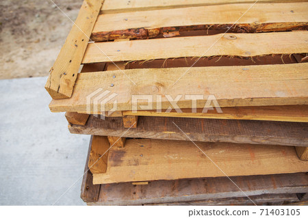 A lot of old wooden pallets stand on the street on top of each other, all for repair. 71403105