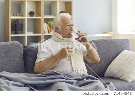 Sick senior man with bad cold or flu sitting on sofa at home and taking medicine with water 71404848