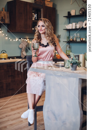 Blonde woman in pink with glass in kitchen. Blonde woman in pink with glass in kitchen. 71405330