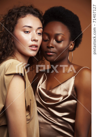 two pretty girls african and caucasian blond posing cheerful together on brown background, ethnicity diverse lifestyle people concept two pretty girls african and caucasian blond posing cheerful together on brown background, ethnicity diverse lifestyle people concept 71407127