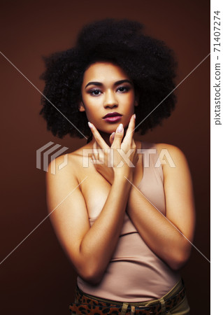 pretty young african american woman with curly hair posing cheerful gesturing on brown background, lifestyle people concept 71407274