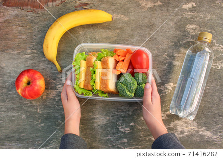 Sandwiches, fruits and vegetables in food box, water on old wooden background. Top view. Sandwiches, fruits and vegetables in food box, water on old wooden background. Top view. 71416282