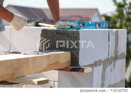 A worker builds the walls of a house from aerated concrete bricks. A worker builds the walls of a house from aerated concrete bricks. 71416795