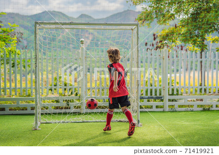 Little cute kid boy in red football uniform playing soccer, football on field, outdoors. Active child making sports with kids or father, Smiling happy boy having fun in summer 71419921