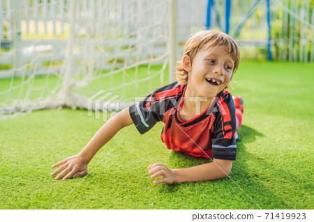 Little cute kid boy in red football uniform playing soccer, football on field, outdoors. Active child making sports with kids or father, Smiling happy boy having fun in summer 71419923
