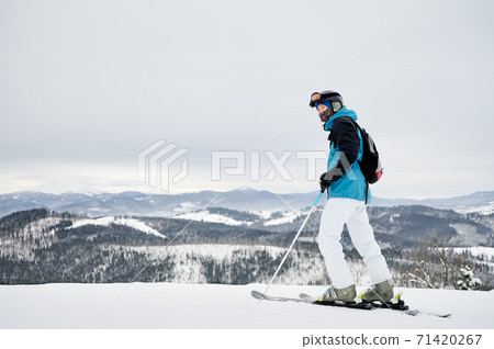Male skier standing on snowy hill in mountains. 71420267