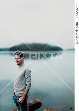 Portrait of young male model on a rainy day with a beautiful lake in the background Portrait of young male model on a rainy day with a beautiful lake in the background 71420745