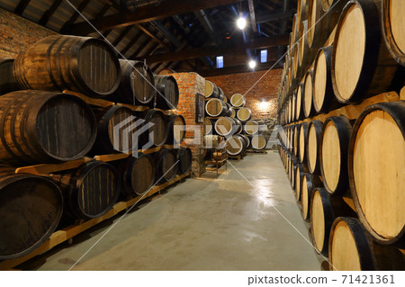Rows of alcoholic barrels are kept in stock. Distillery. Cognac, whiskey, wine, brandy. Alcohol in barrels, alcohol storage 71421361