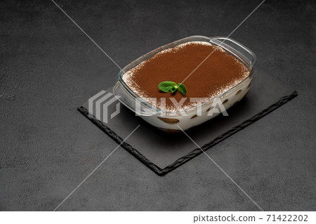 Traditional Italian Tiramisu dessert in glass baking dish on stone serving board on concrete background 71422202
