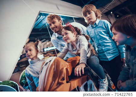 Dad and children watch as girl drives motorcycle. Dad and children watch as girl drives motorcycle. 71422765