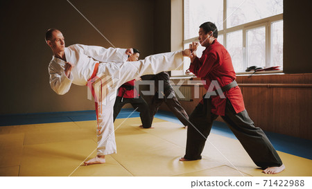 Bald man kicks his opponent in the karate hall.  71422988