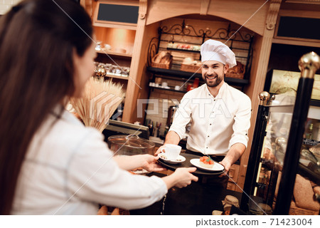 Young Man Selling Cakes and Tea to Woman in Bakery Young Man Selling Cakes and Tea to Woman in Bakery 71423004