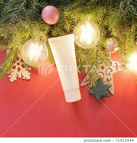 Unbranded white squeeze cosmetic tube, fir tree, stars, balls and magic lights on red background with copy space. Top view, flatlay style, mock-up. 71423444