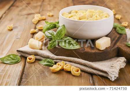 Tortellini mignon on a wooden board with basil and parmesan. Specialties of the cuisine from Bologna Tortellini mignon on a wooden board with basil and parmesan. Specialties of the cuisine from Bologna 71424730