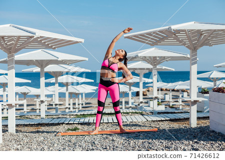 Beautiful brunette woman sports fitness gymnastics on the beach by the sea in the morning Beautiful brunette woman sports fitness gymnastics on the beach by the sea in the morning 71426612