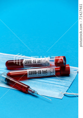 Syringe, test tube with blood sample and disposable face mask to prevent COVID-19 virus on blue background Syringe, test tube with blood sample and disposable face mask to prevent COVID-19 virus on blue background 71427481