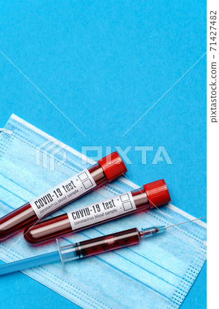 Syringe, test tube with blood sample and disposable face mask to prevent COVID-19 virus on blue background 71427482