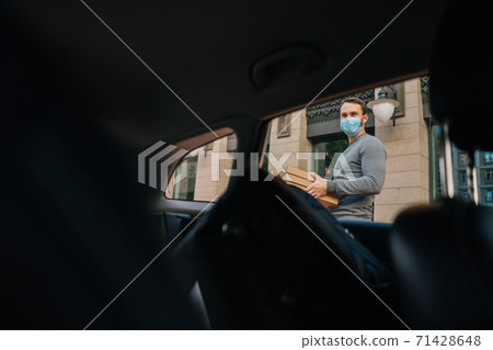Shooting from interior car of delivery man wearing medical protective mask holding boxes with pizza. 71428648