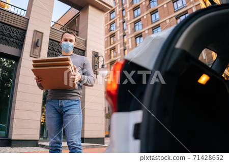 Low-angle shot of delivery man wearing medical protective mask holding carton boxes with hot pizza. 71428652