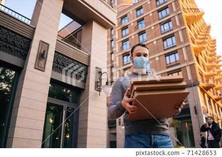 Low-angle shot of delivery man wearing medical protective mask holding carton boxes with hot pizza. 71428653