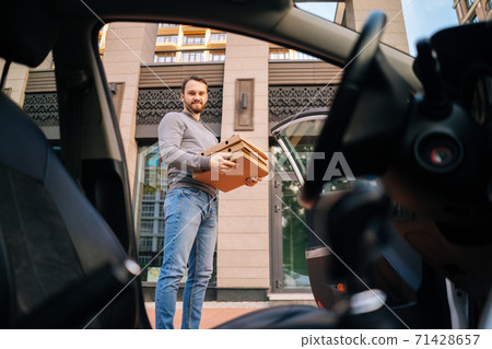 Bearded handsome Caucasian delivery man standing at city street and holding carton boxes with food.  71428657