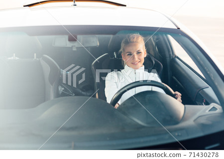 Beautiful fashionable blonde woman behind the wheel of a white car 71430278