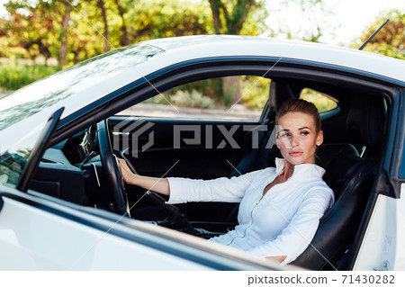Beautiful female blonde driver behind the wheel of a white car 71430282
