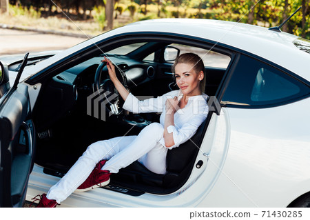 Beautiful female blonde driver behind the wheel of a white car Beautiful female blonde driver behind the wheel of a white car 71430285