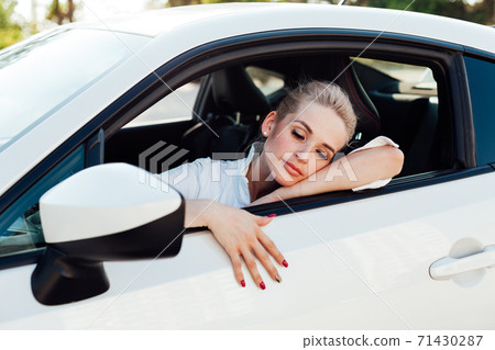 Beautiful female blonde driver behind the wheel of a white car 71430287