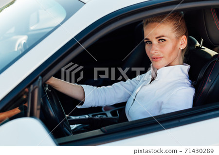 Beautiful female blonde driver behind the wheel of a white car Beautiful female blonde driver behind the wheel of a white car 71430289