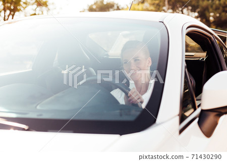 Beautiful female blonde driver behind the wheel of a white car Beautiful female blonde driver behind the wheel of a white car 71430290