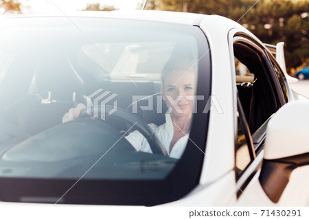 Beautiful female blonde driver behind the wheel of a white car 71430291