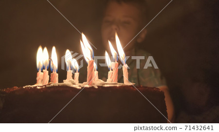 Cute boy blows out candles on a cake on his birthday. Happy child looks at a cake with candles. Happiness concept Cute boy blows out candles on a cake on his birthday. Happy child looks at a cake with candles. Happiness concept 71432641