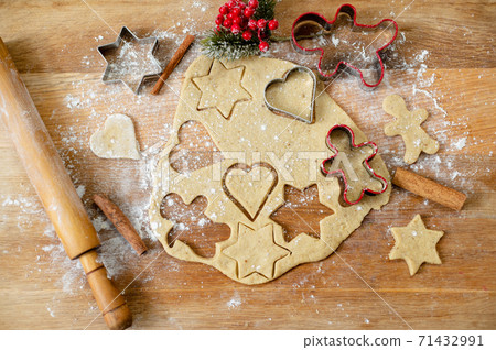Still life, a top view of a kitchen board with rolled out dough, raw gingerbread preparations, cinnamon sticks and Christmas decoration. 71432991
