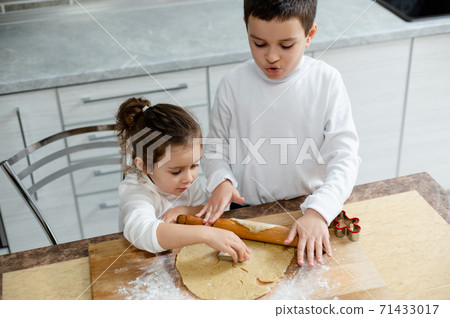 Children will cut from the tesca of the blank for Christmas cookies with the assistants of special forms. Children cook cookies in their kitchen. Children will cut from the tesca of the blank for Christmas cookies with the assistants of special forms. Children cook cookies in their kitchen. 71433017