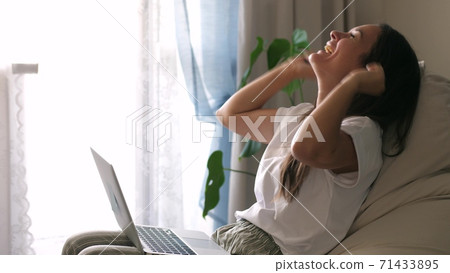 Excited young woman winner looks at laptop celebrates online success sits on sofa at home. Girl gets new distance job opportunity, reads good news in email, rejoices victory, feels motivated. 71433895