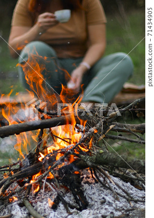 Bonfire in spring forest. Fire coal forest. Young girl drinking a hot drink in the background, shallow depth of field Bonfire in spring forest. Fire coal forest. Young girl drinking a hot drink in the background, shallow depth of field 71434905