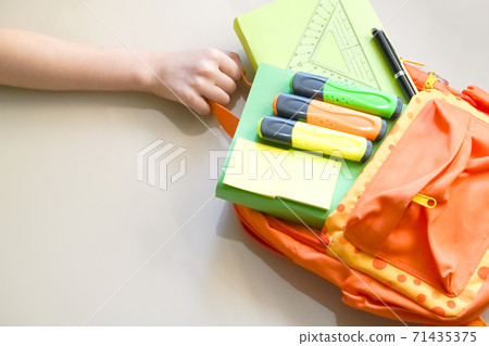 Hand holds orange backpack with school supplies. Back to School 71435375