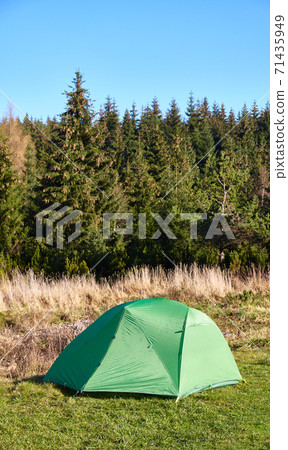 Green tent on a meadow by the edge of a mountain forest. 71435949
