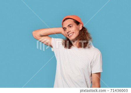Freestyle. Curly-haired guy wearing hat standing isolated on blue looking aside smiling joyful Freestyle. Curly-haired guy wearing hat standing isolated on blue looking aside smiling joyful 71436003
